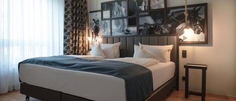 Een moderne slaapkamer met een groot bed, een hoofdbord met kunst, een nachtkastje en een hanglamp.
