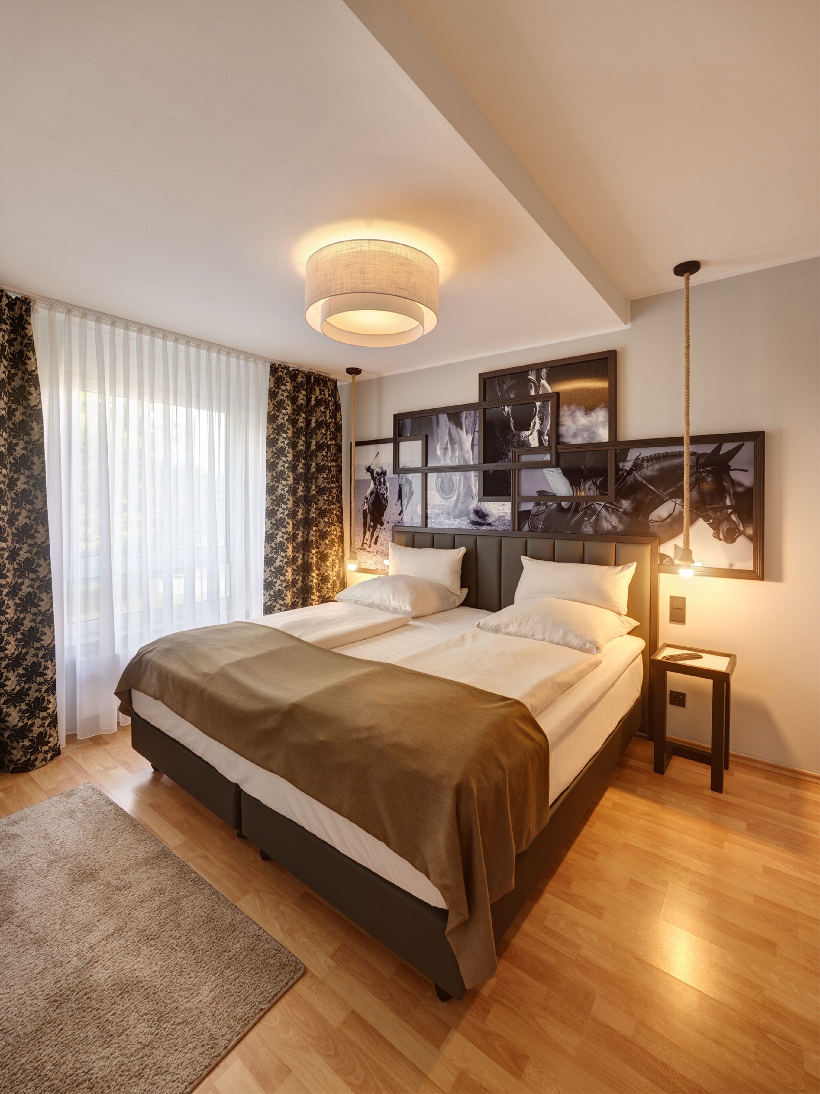 A modern bedroom with a large bed, a bedside table, a floor lamp, and a wall with framed pictures.