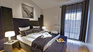 A modern hotel room with a large bed, bedside tables, a bench, and a view of the outdoors.