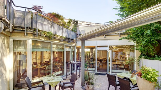 An outdoor patio area with tables and chairs, glass doors leading to an interior dining area, and a metal fence.