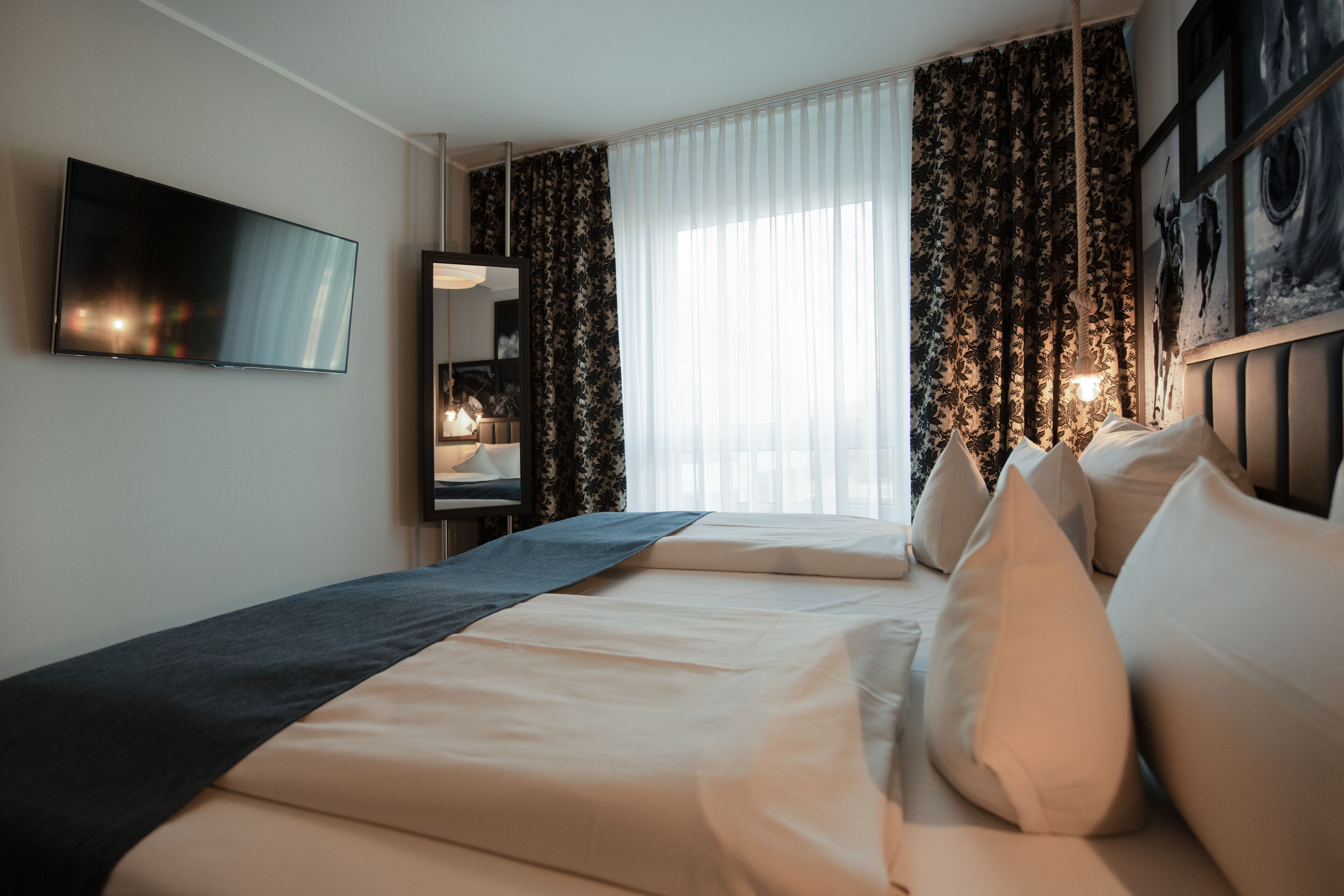 A hotel room with a bed, a TV, a mirror, and a window with curtains.
