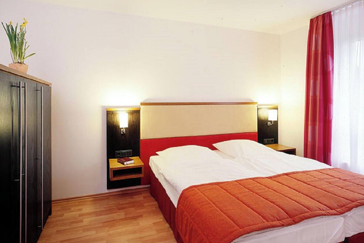 Une chambre d’hôtel avec un lit, un plancher en bois, des tables de chevet, une lampe, une armoire et une fenêtre avec des rideaux.