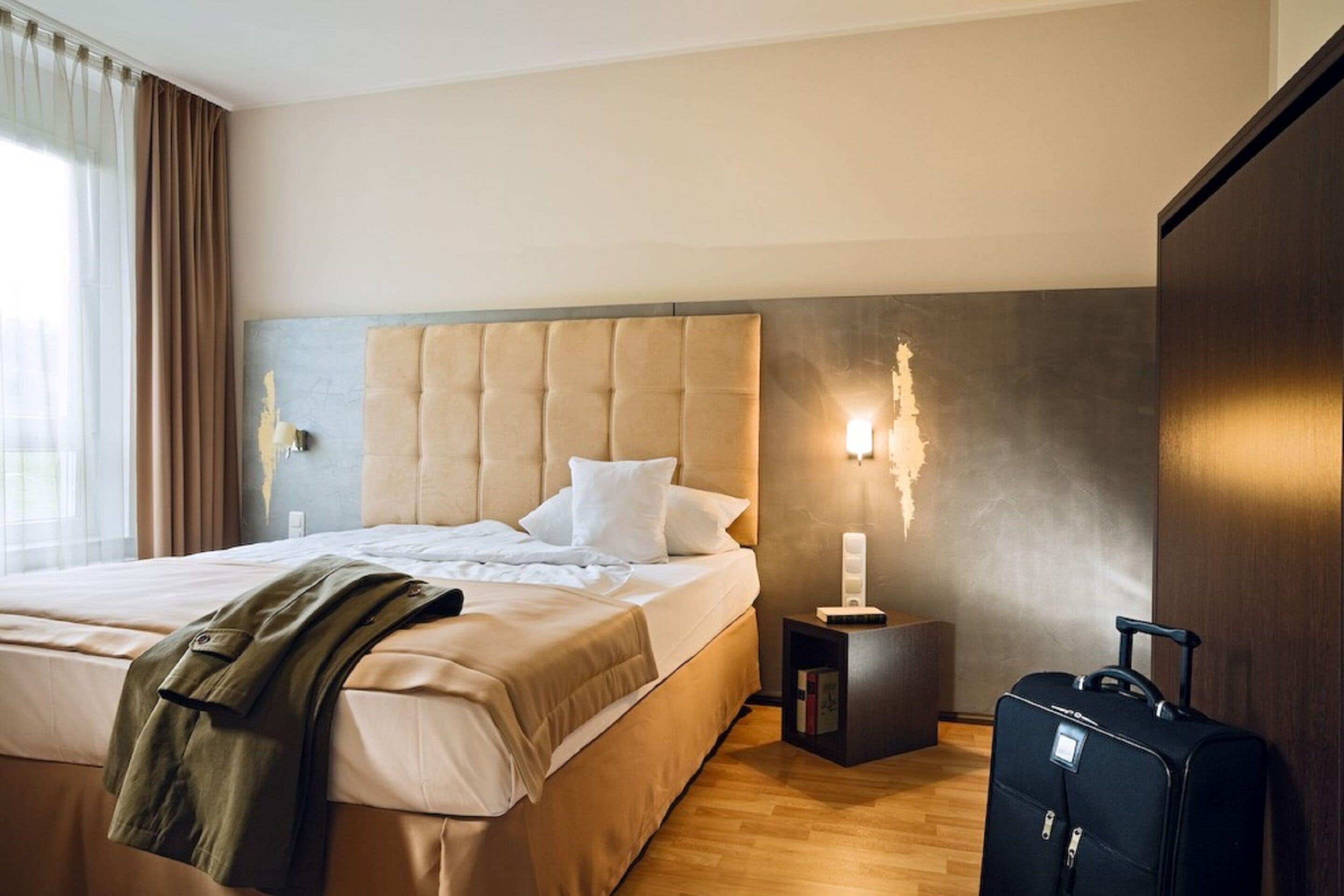 A hotel room with a large bed, a nightstand with a lamp, and a suitcase.