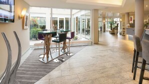 A spacious hotel lobby with a modern dining area, large windows, and a view of the outdoors.