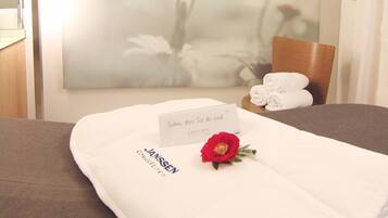 Habitación de hotel con cama, un cuadro de flores colgado en la pared, una tarjeta de nombre y una rosa roja sobre la cama.