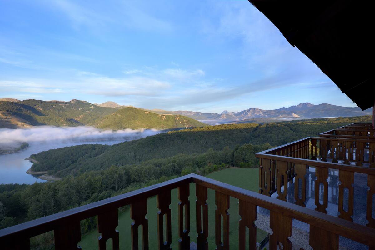 Un balcón con vistas a un paisaje montañoso, un lago y un valle boscoso.