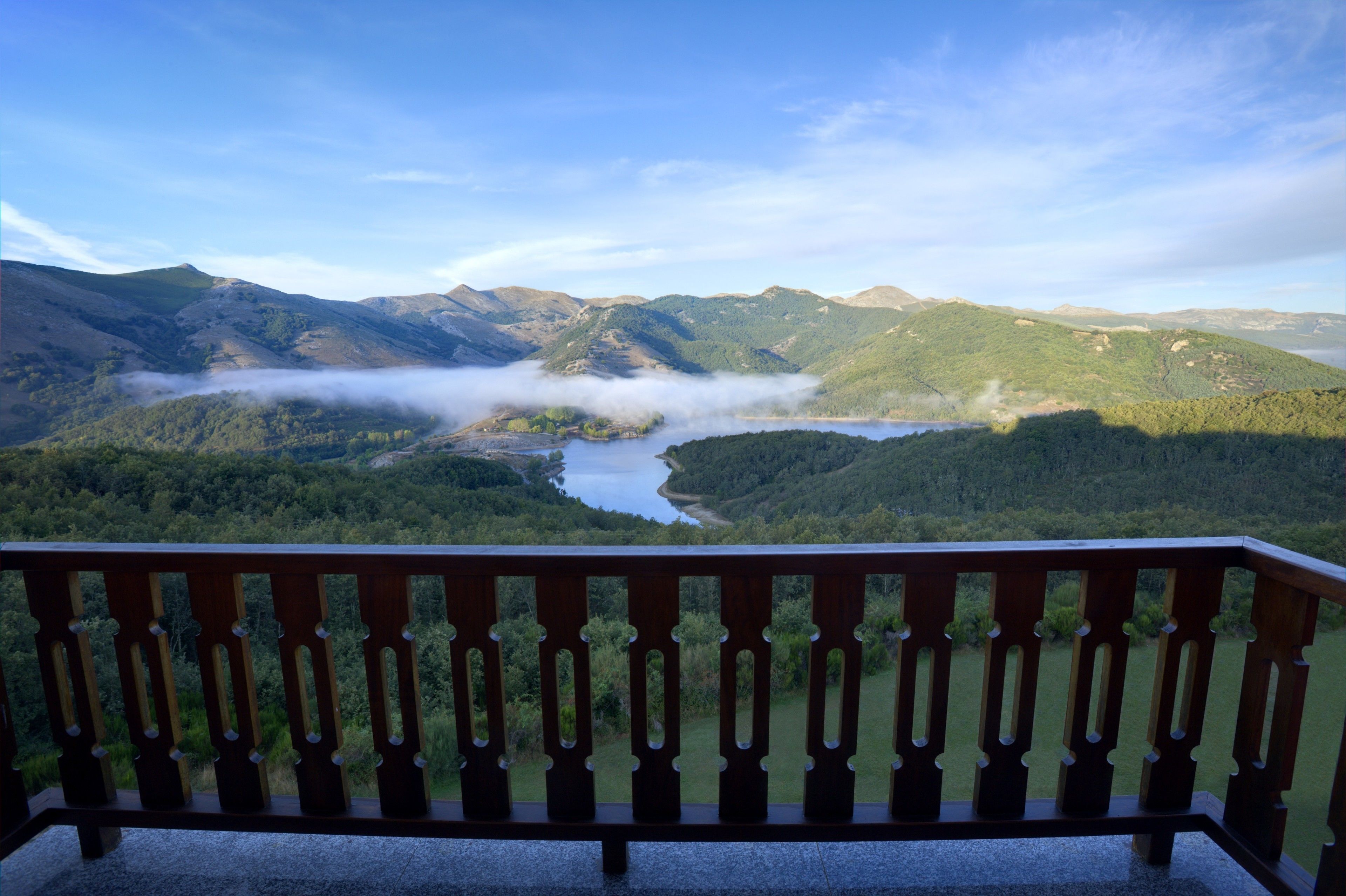 A balcony with a view of a valley, mountains, and a lake.
