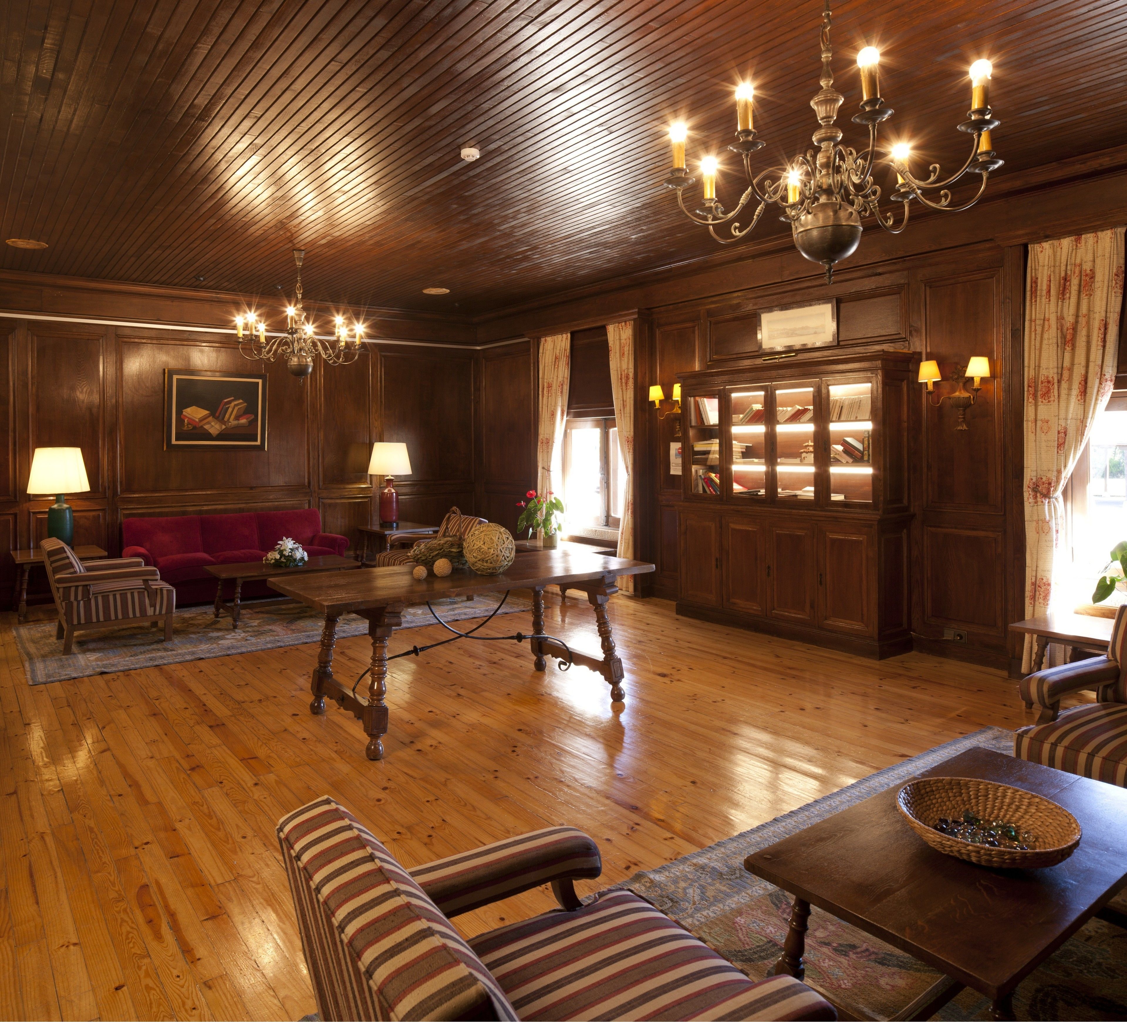 A traditional room with wooden floors, a red sofa, striped armchairs, a wooden coffee table, and a chandelier.