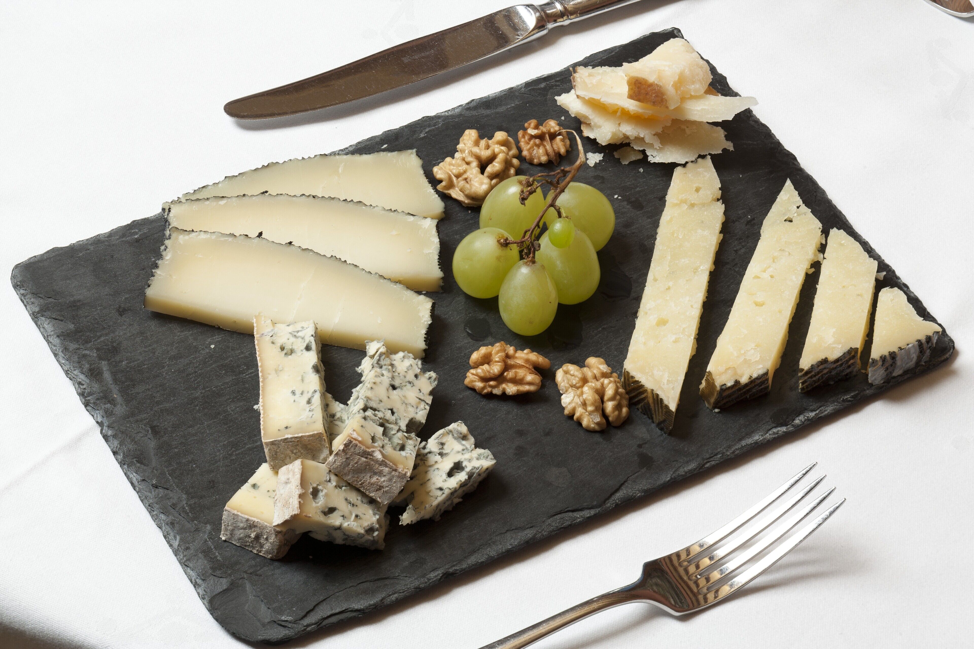 A slate board with various cheeses, grapes, and walnuts.