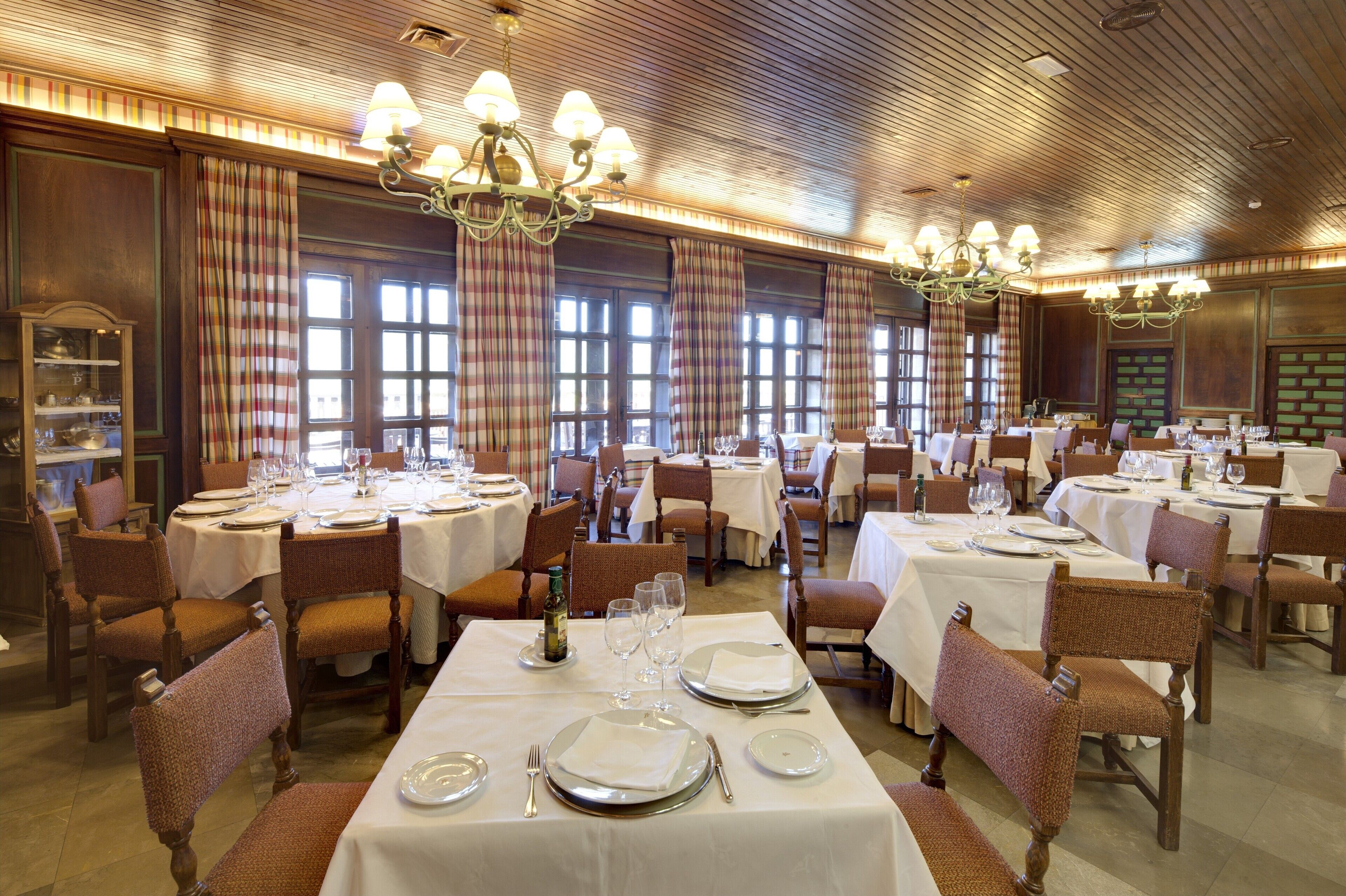 Un comedor formal con varias mesas dispuestas para el servicio, paredes cubiertas de paneles de madera y ventanas amplias.