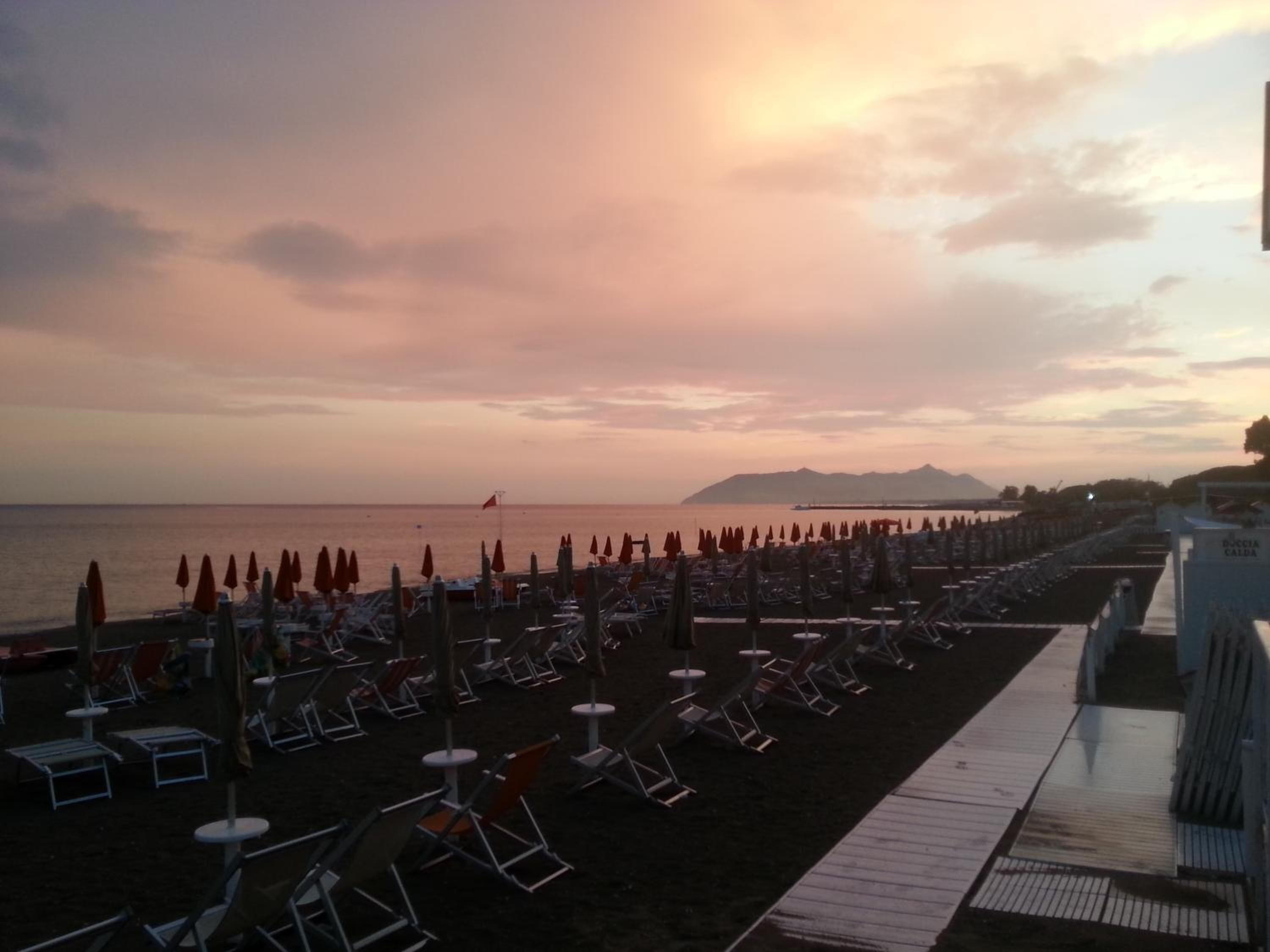 A beach with rows of sun loungers and umbrellas, a wooden walkway, and a calm sea.