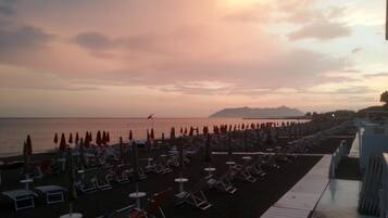 A beach with rows of sun loungers and umbrellas, a wooden walkway, and a calm sea.