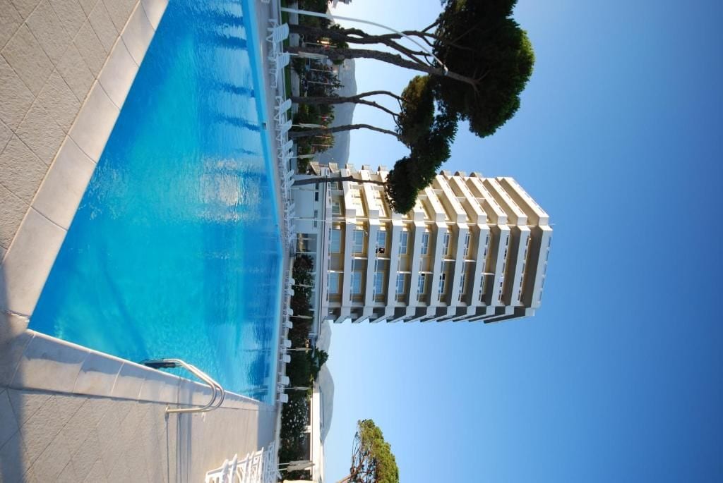 A swimming pool adjacent to a hotel with a clear blue sky.