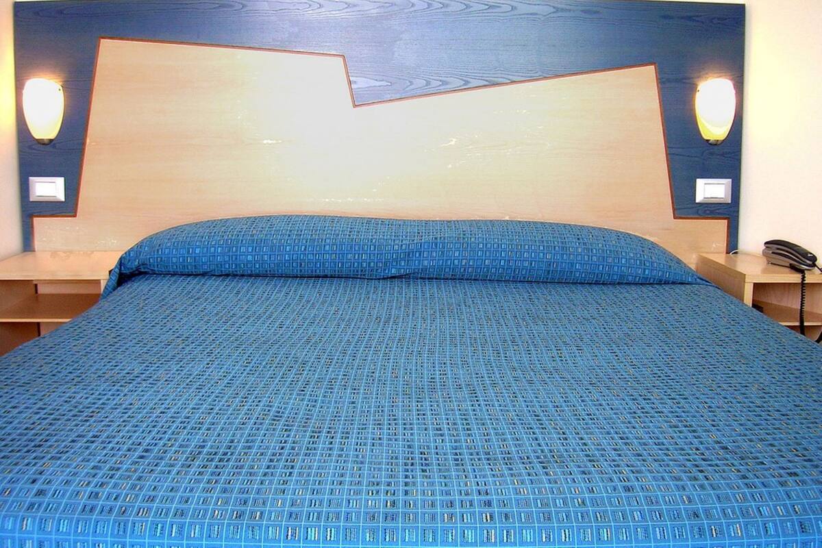 A hotel room with a large bed, a wooden headboard, two bedside tables, and a telephone on one of the tables.