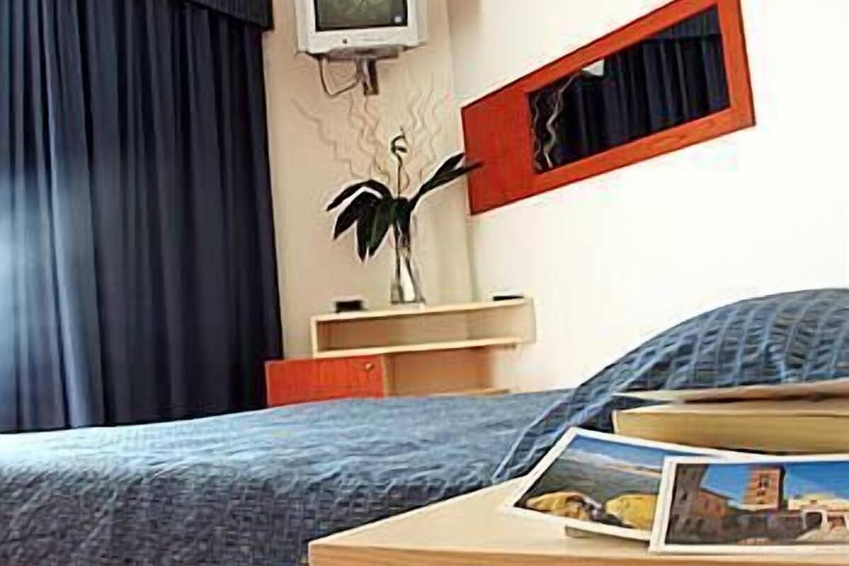 A bedroom with a bed, a TV mounted on the wall, a mirror, and a bedside table with a photo frame.