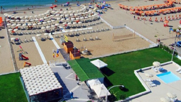 Ett semesterhotell vid stranden med en rund sittgrupp, en pool och en byggnad med ett sluttande tak.