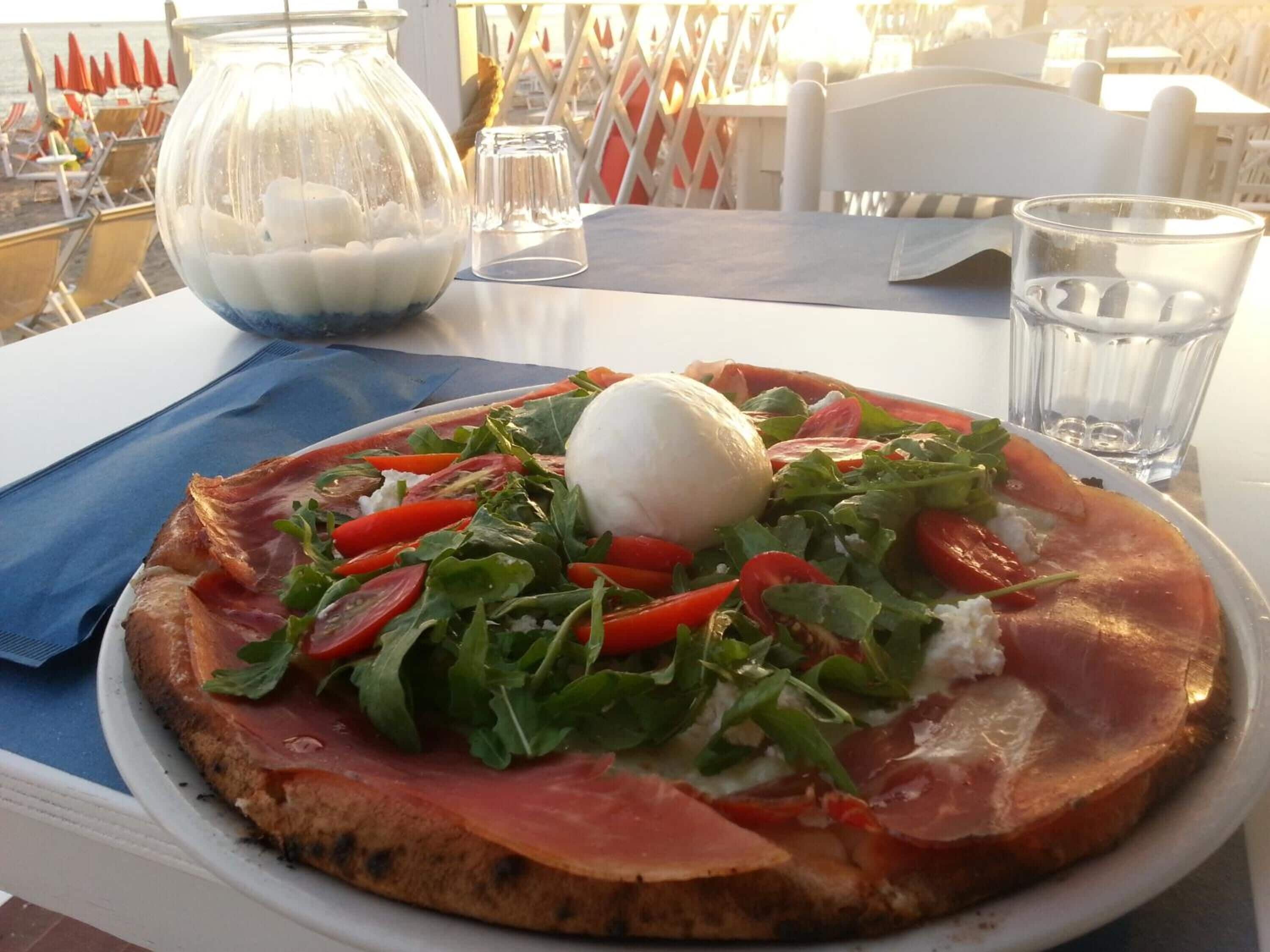 Pizza con rucola, pomodori e una pallina di mozzarella su un piatto bianco.