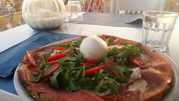 Pizza con rucola, pomodori e una pallina di mozzarella su un piatto bianco.