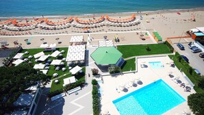 En vy från ovan över ett semesterområde med en swimmingpool, solstolar och en strand med parasoller.
