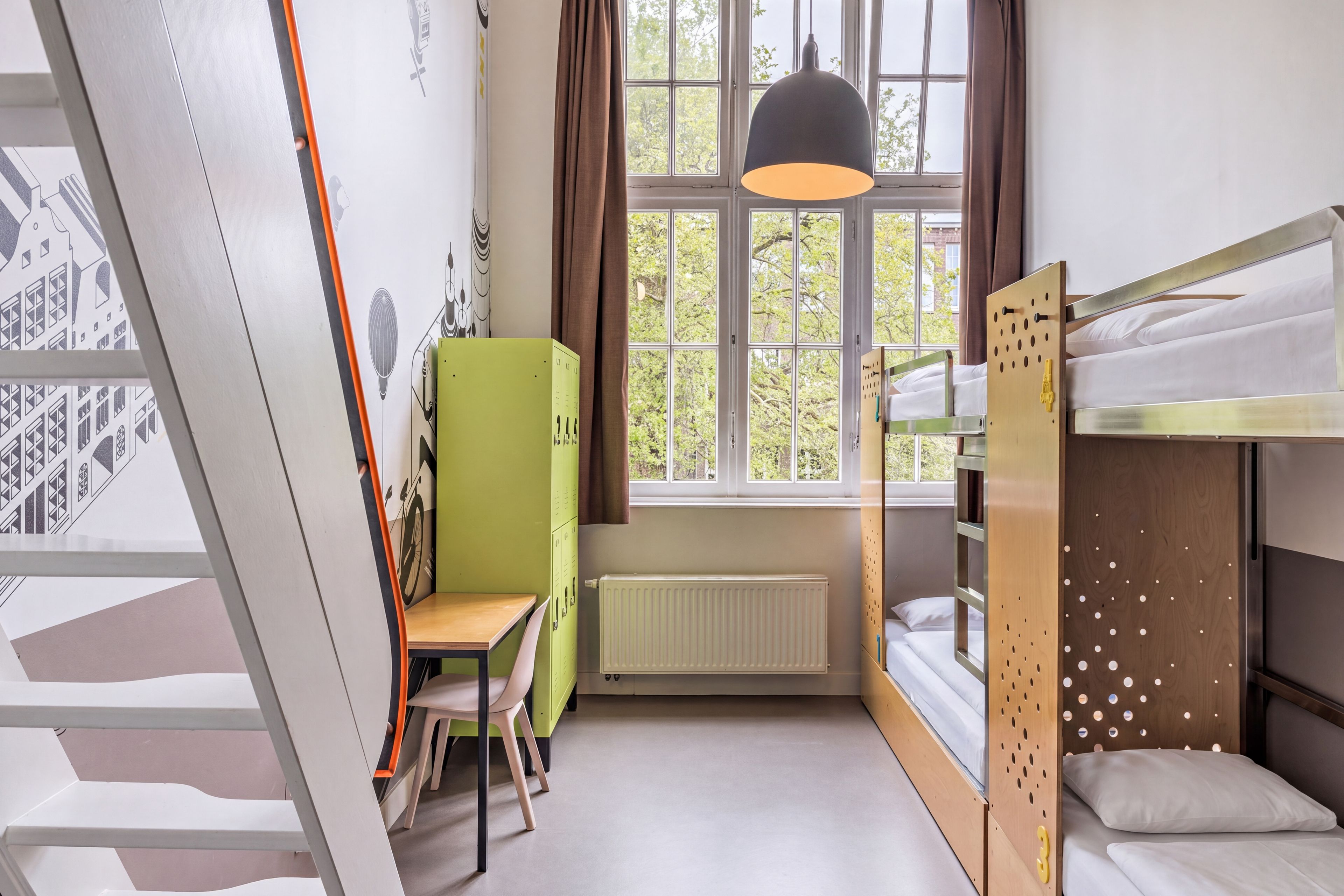 Een stapelbed met een houten hoofdbord, een bureau met een stoel, een radiator en een raam met gordijnen.