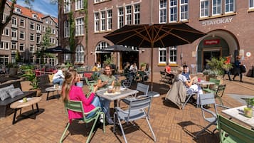 An outdoor cafe area with tables and chairs, surrounded by brick buildings and a Stayokay sign.