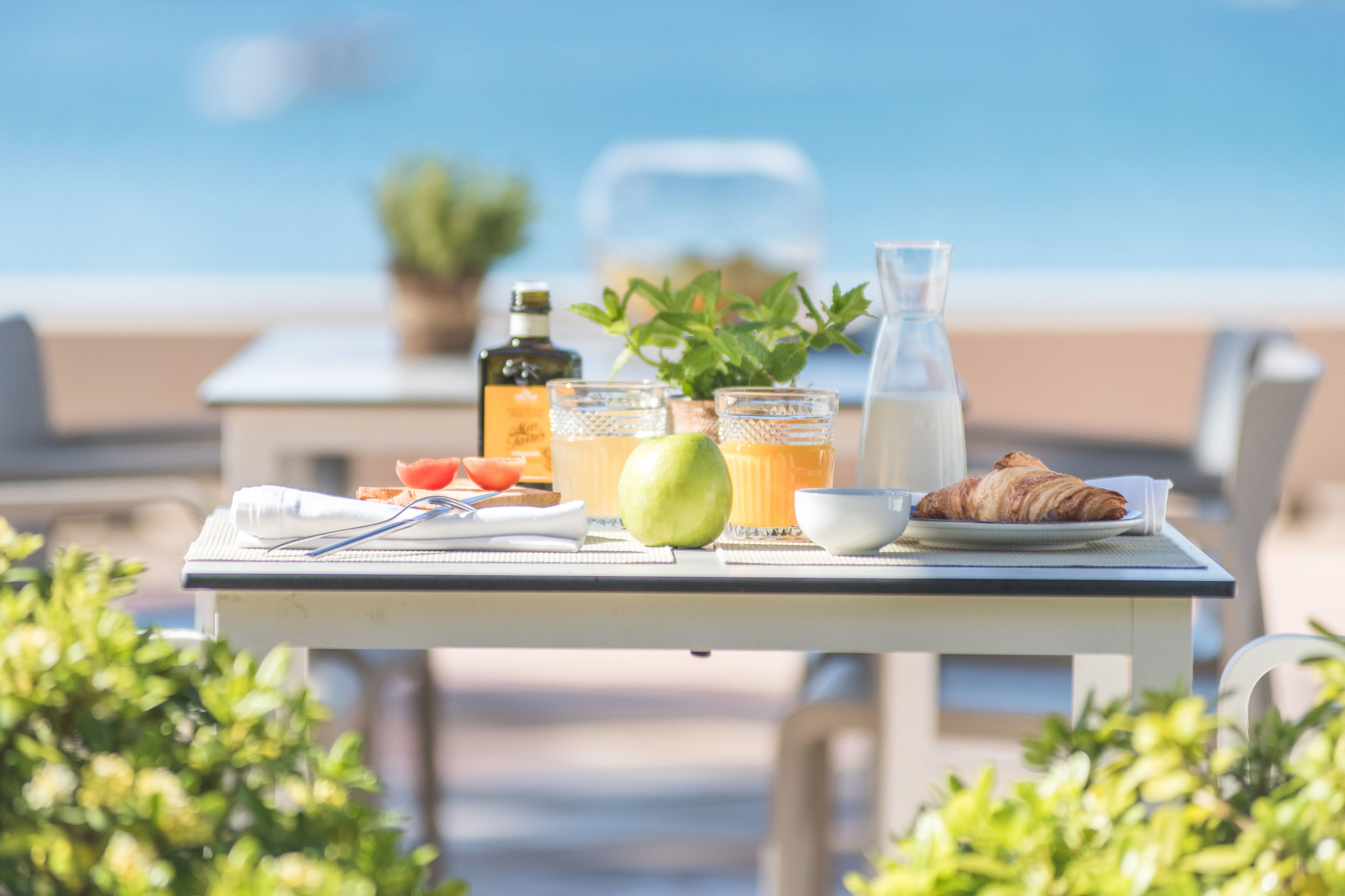 A table set with breakfast items, including a croissant, fruit, and beverages, overlooking a beach.