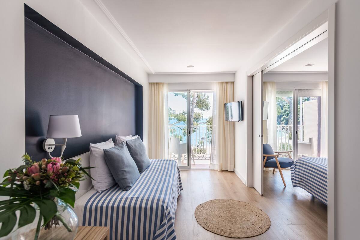 A modern bedroom with a large bed, a bedside table with a lamp, and a view of the balcony.