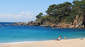 Une plage avec une eau d’un bleu limpide, des falaises rocheuses et des arbres.