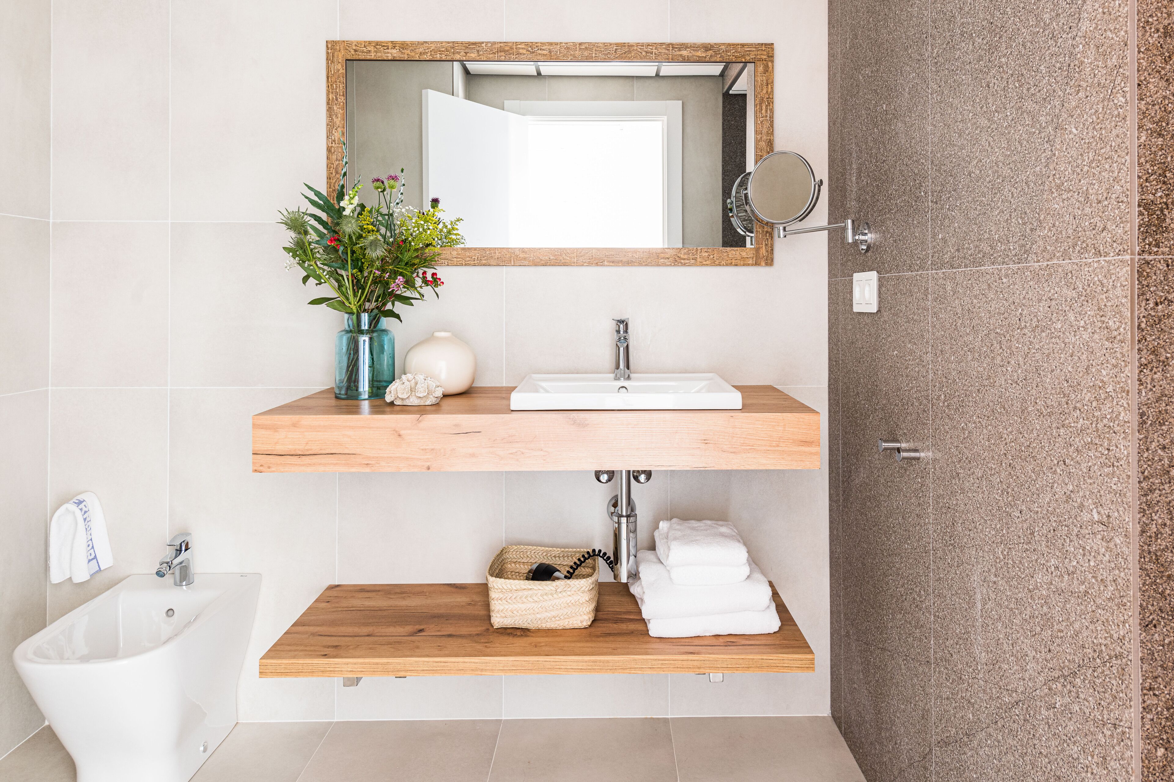 A modern bathroom with a wooden vanity, a white sink, a bidet, and a mirror.