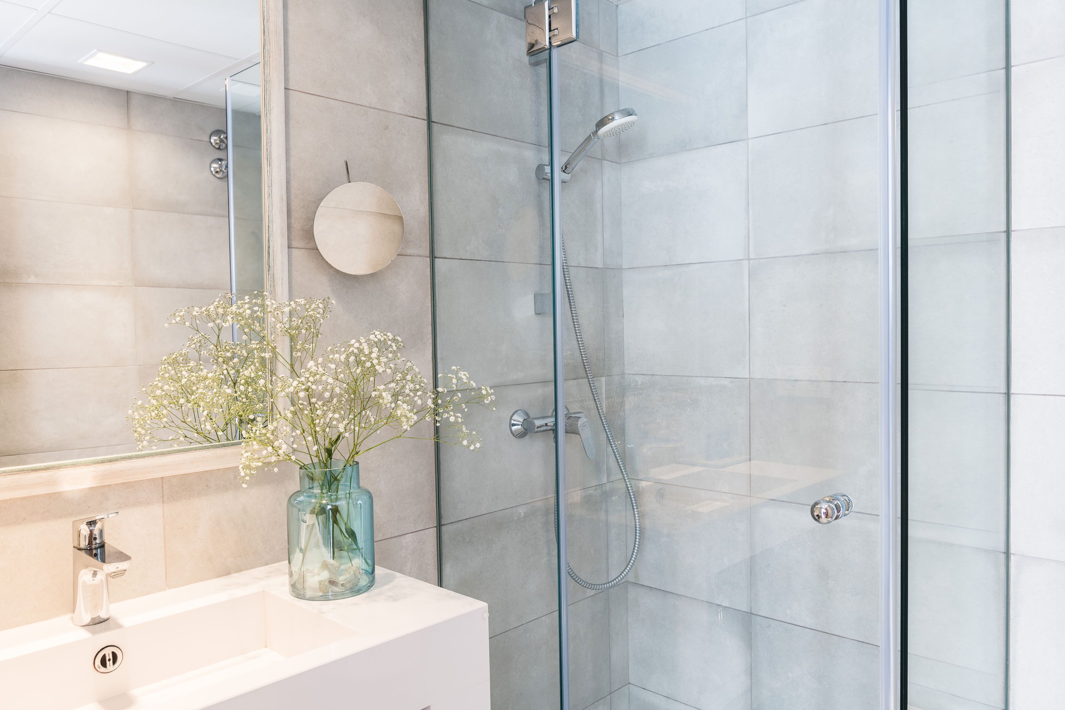 A modern bathroom with a glass-enclosed shower, a white sink, and a vase with flowers.
