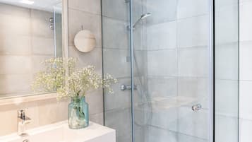 A modern bathroom with a glass-enclosed shower, a white sink, and a vase with flowers.