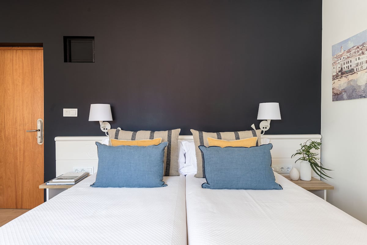 A double bed with white bedding, two blue pillows, and a small bedside table with a lamp.
