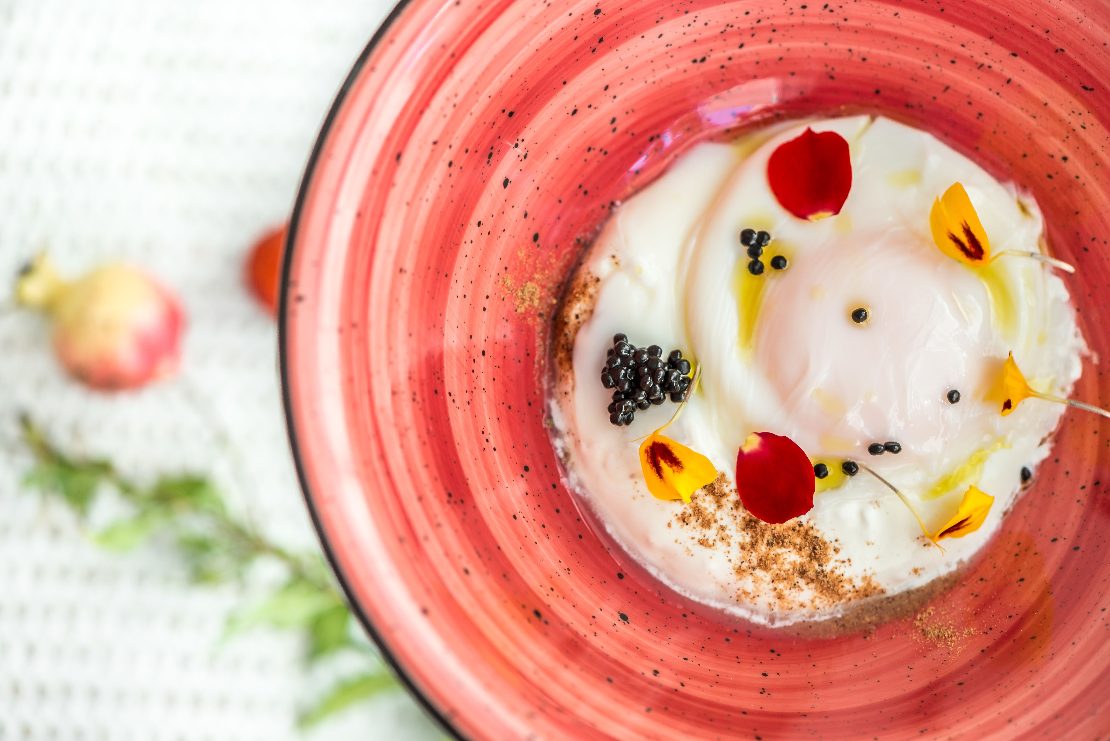 A close-up of a dessert with a creamy white base, garnished with blackberries, red rose petals, and yellow flowers, served in a pink bowl.
