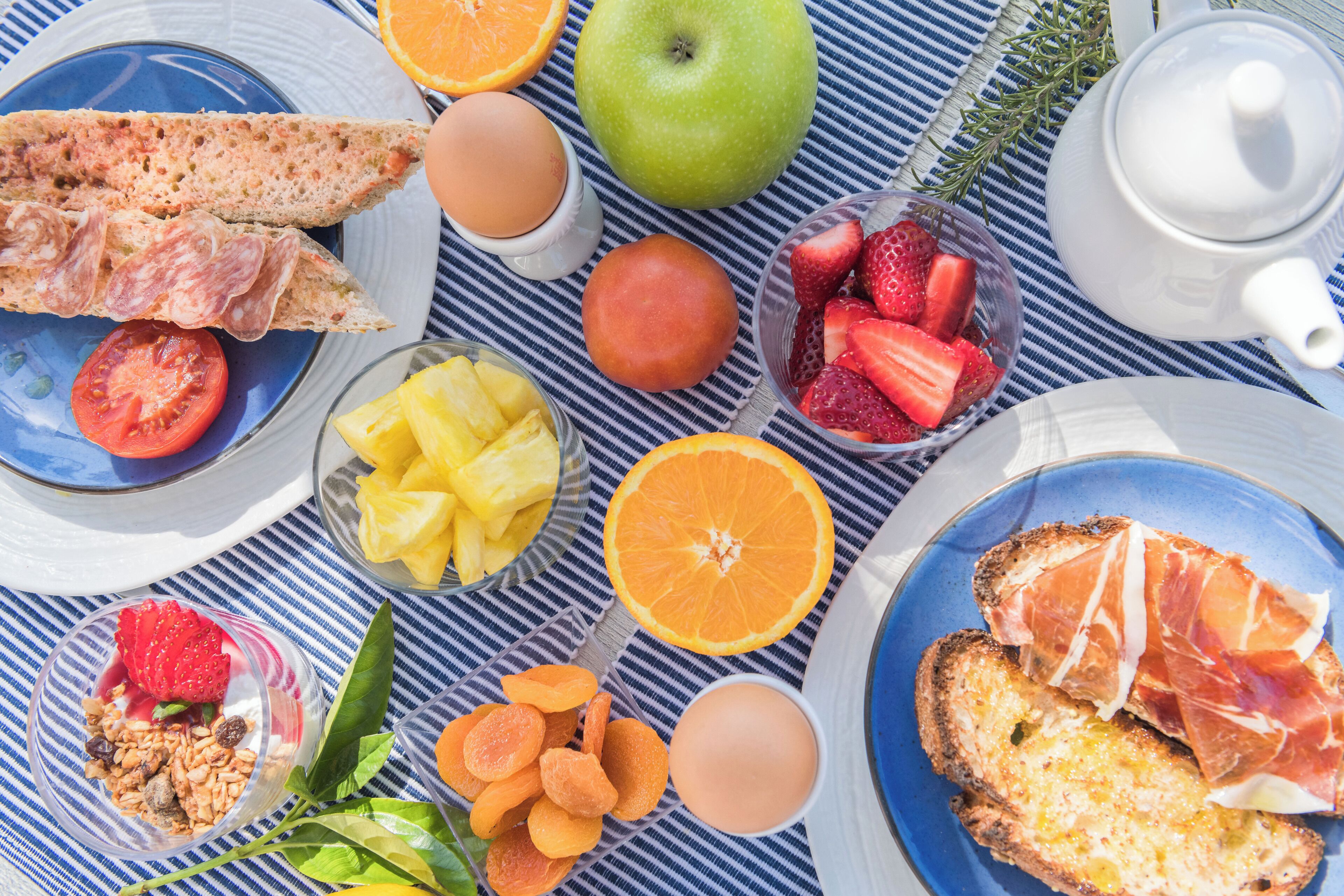 Una mesa de desayuno con diversos alimentos, como pan, huevos, frutas y una tetera.