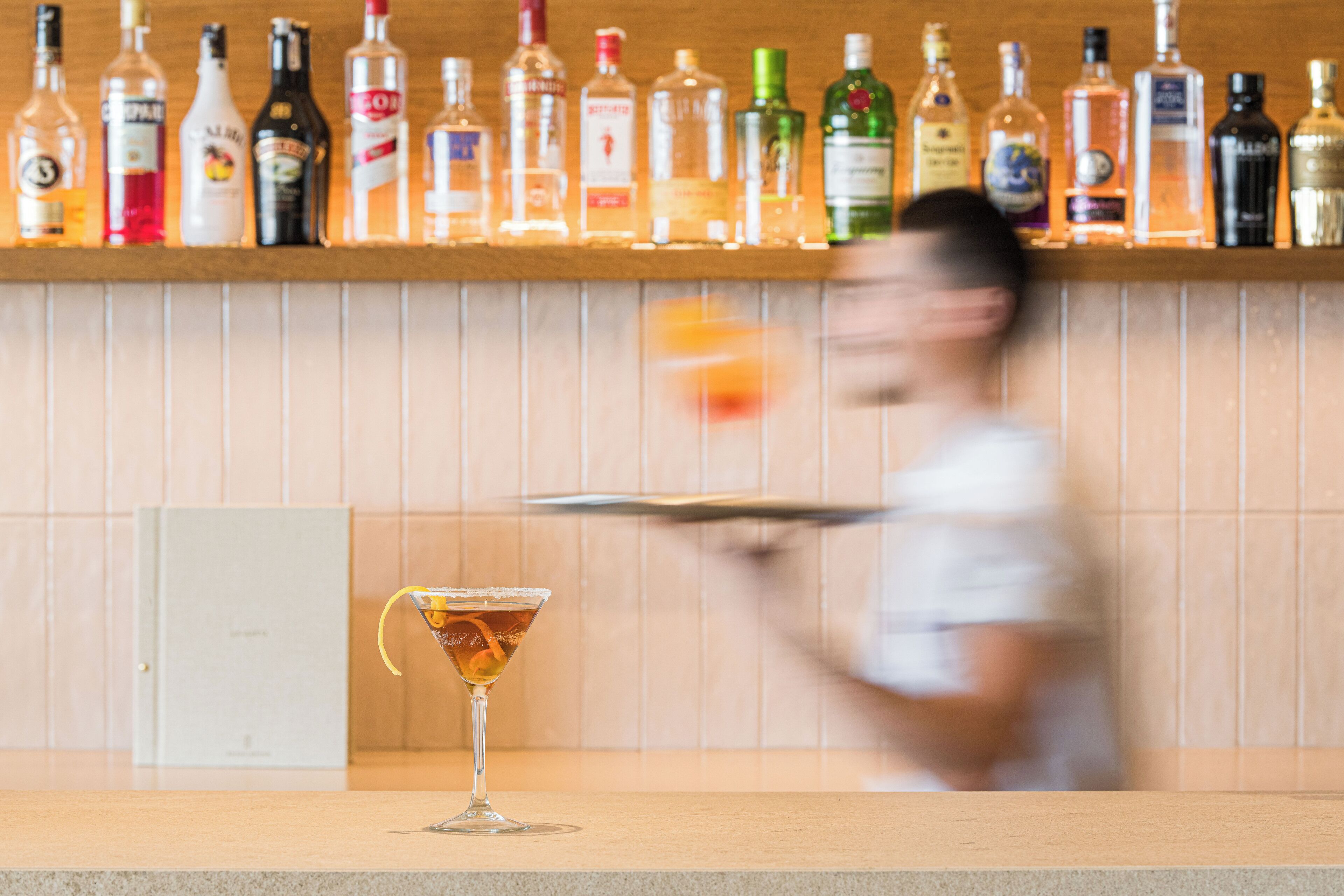 Zona de bar con varias botellas de licor en estanterías y una copa de martini en la barra.