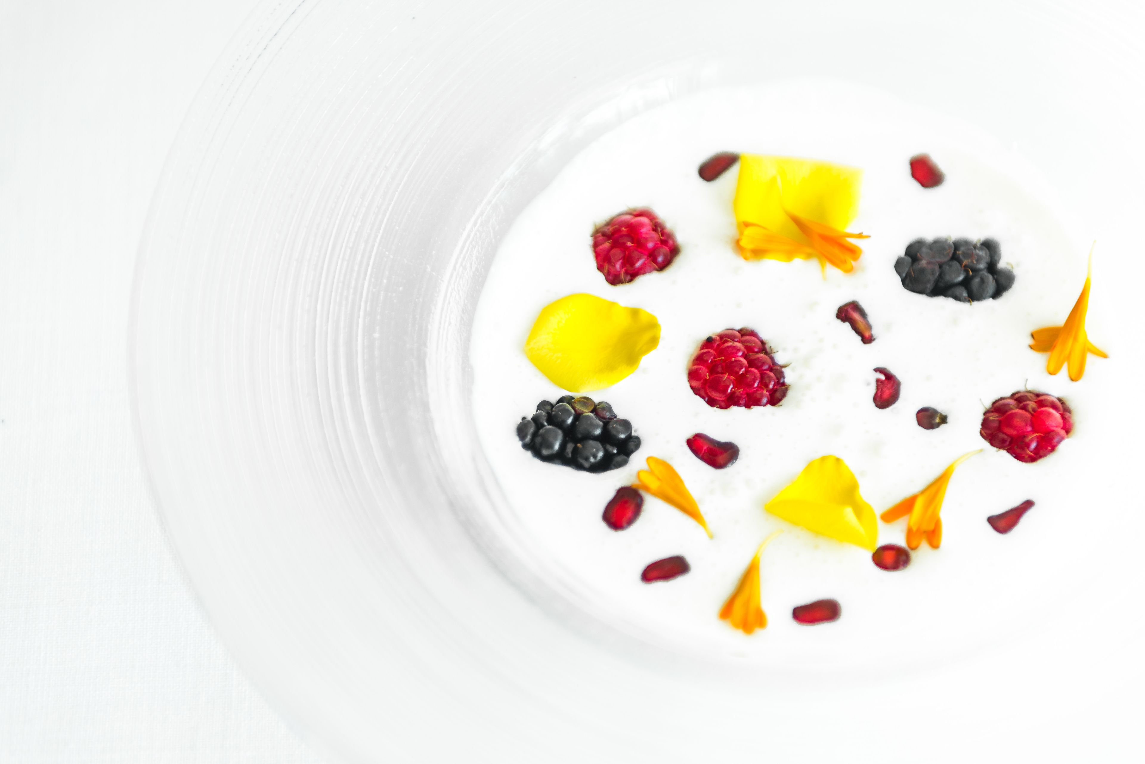 A white bowl with a creamy dessert topped with various fruits and edible flowers.