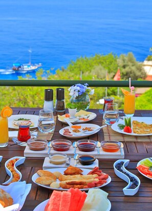 A table set with various dishes, drinks, and condiments, overlooking a body of water with boats. - Diva Residence Hotel (Kas)