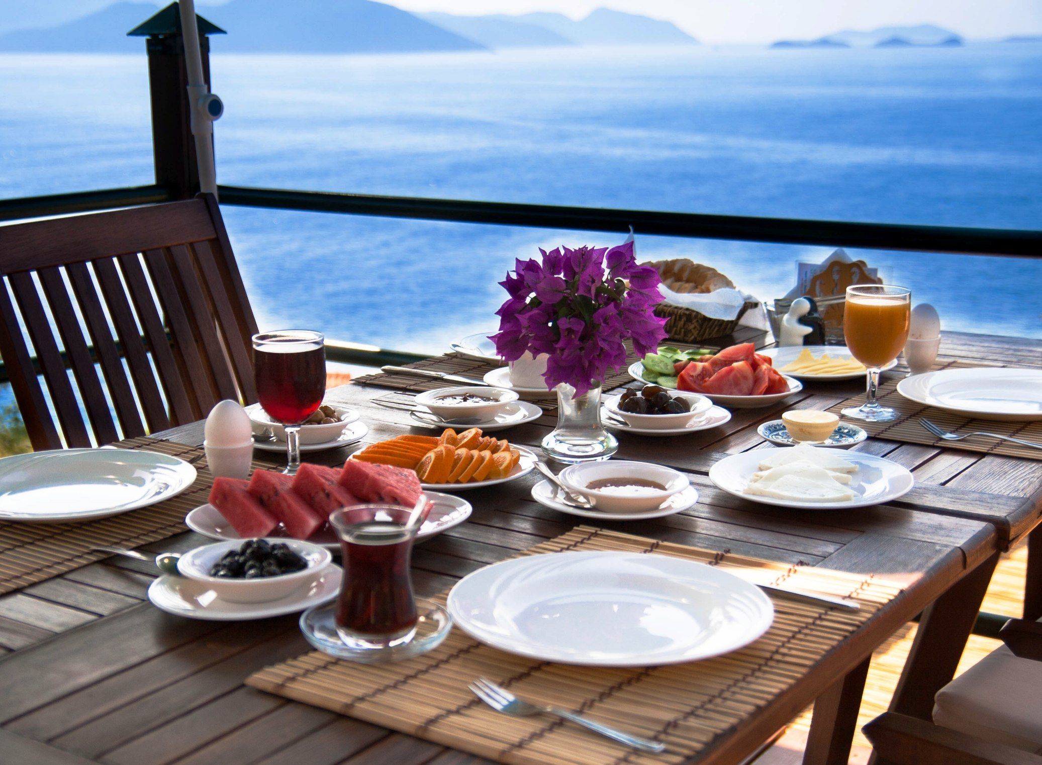 A table set for breakfast with various dishes, a glass of red wine, and a view of the sea.