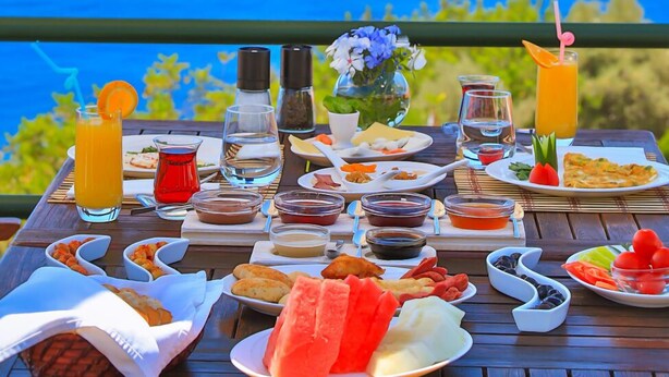 A table set with a variety of food and drinks, overlooking a scenic ocean view. - Diva Residence Hotel (Kas)