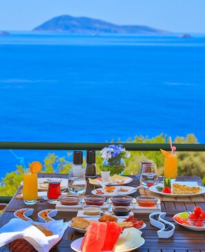 Mesa dispuesta con diversos alimentos y bebidas, con vistas a un paisaje marino.