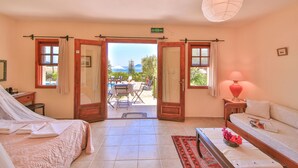 A room with a bed, a sofa, a table with a lamp, and an open door leading to an outdoor area with a table and chairs. - Diva Residence Hotel (Kas)