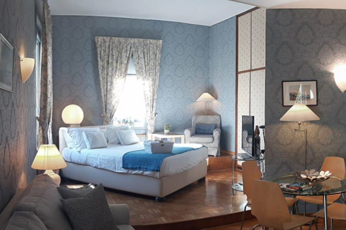 A hotel room with a bed, a desk, a chair, a lamp, and a wardrobe.