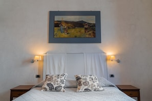 Een keurig opgemaakt bed met patroon kussens, een schilderij erboven en twee bedlampen.