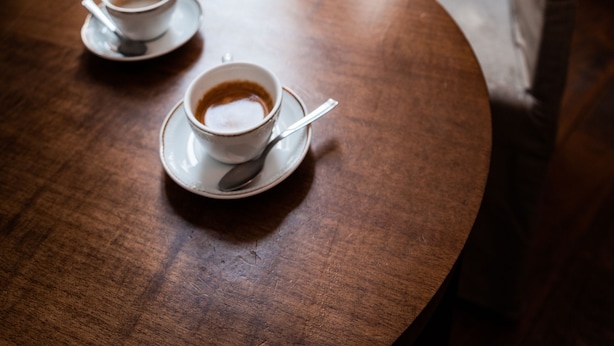 A round wooden table with two white cups of coffee and saucers, a beige armchair, and a view of a building through a wooden door. - Il Salotto di Firenze (Florence)