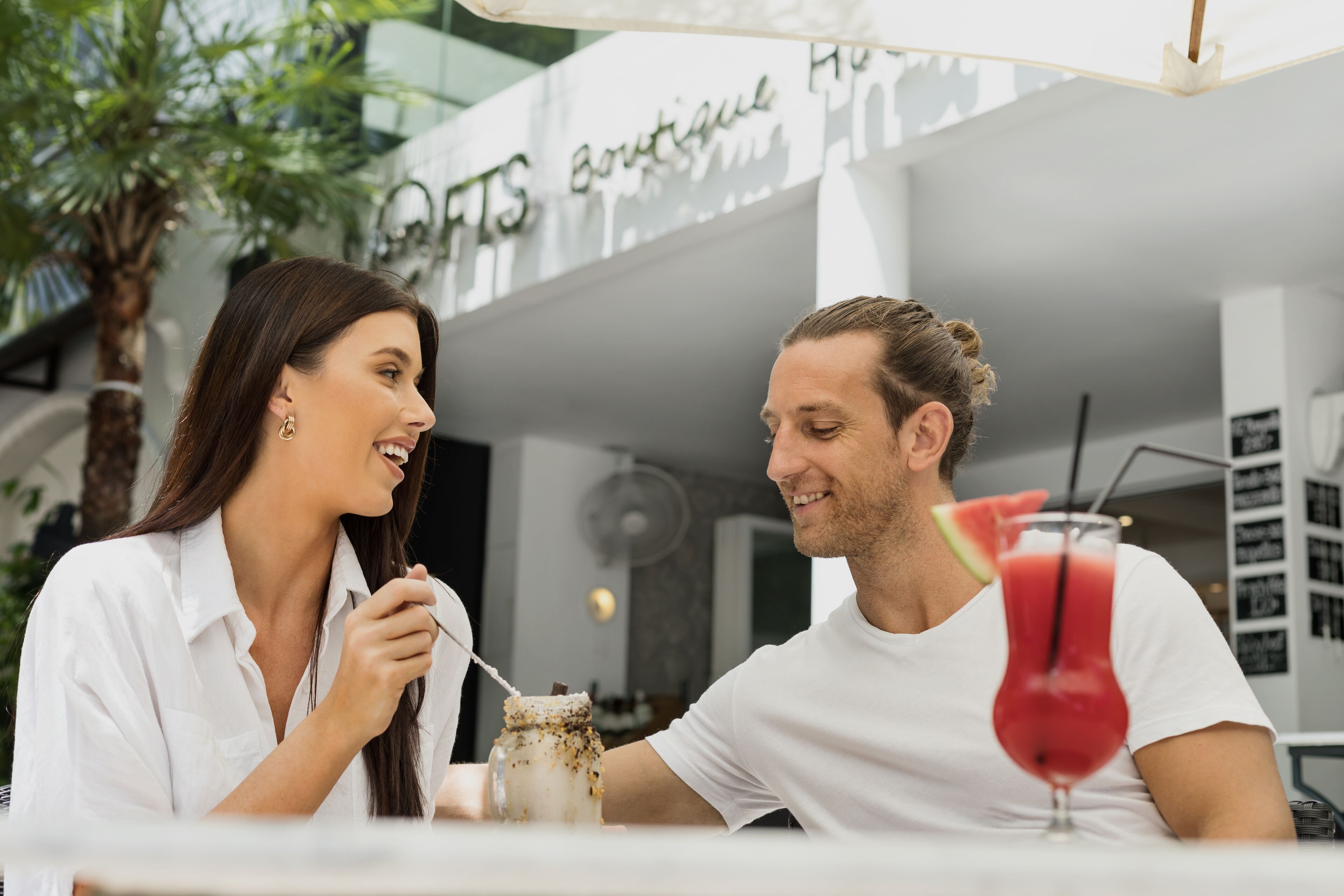 Two people sitting at an outdoor table with a drink and a jar of dessert in front of them.