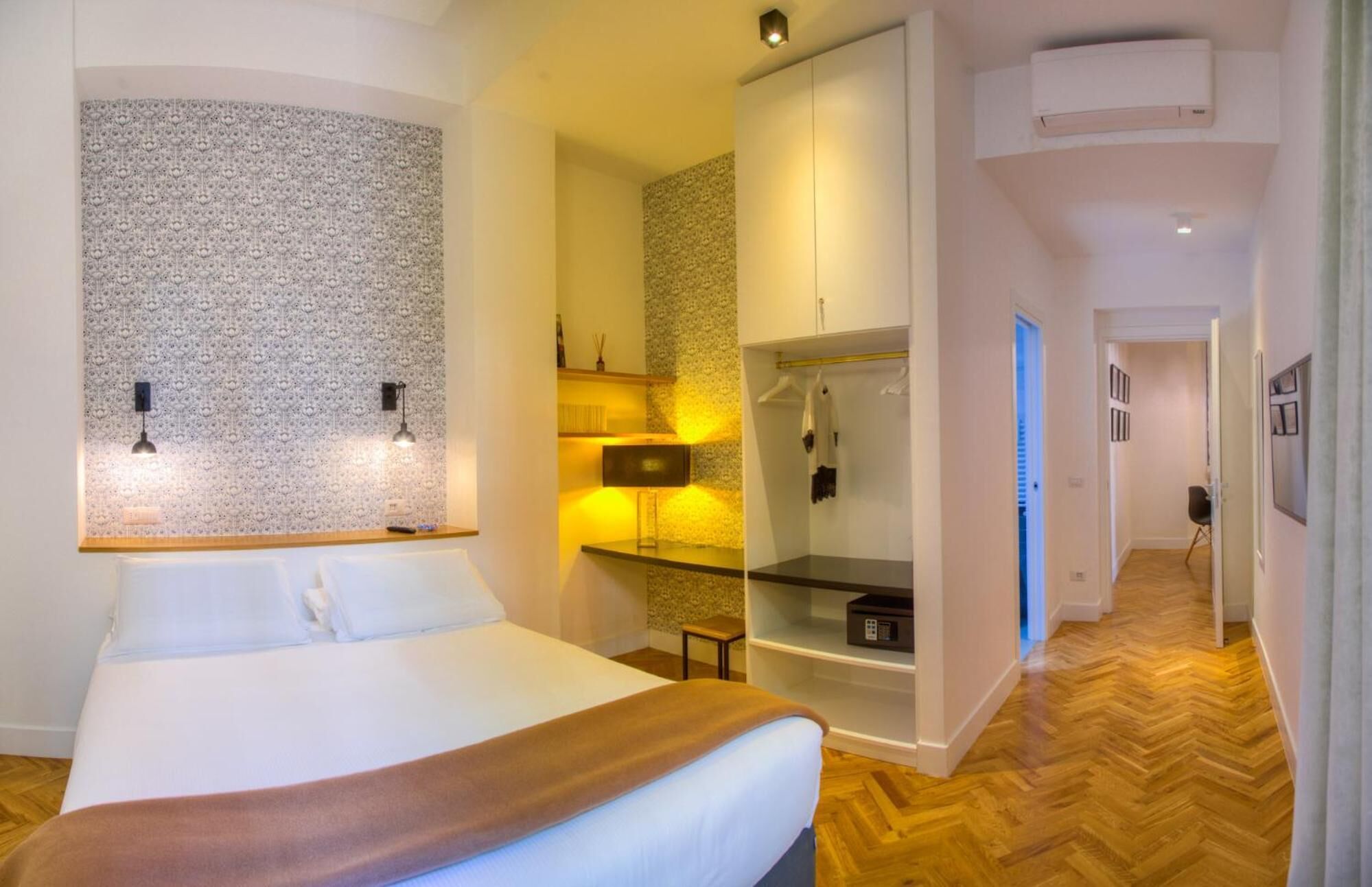 Ein Hotelzimmer mit Bett, Schrank, Spiegel, Ablage für Toilettenartikel und einem Flur.