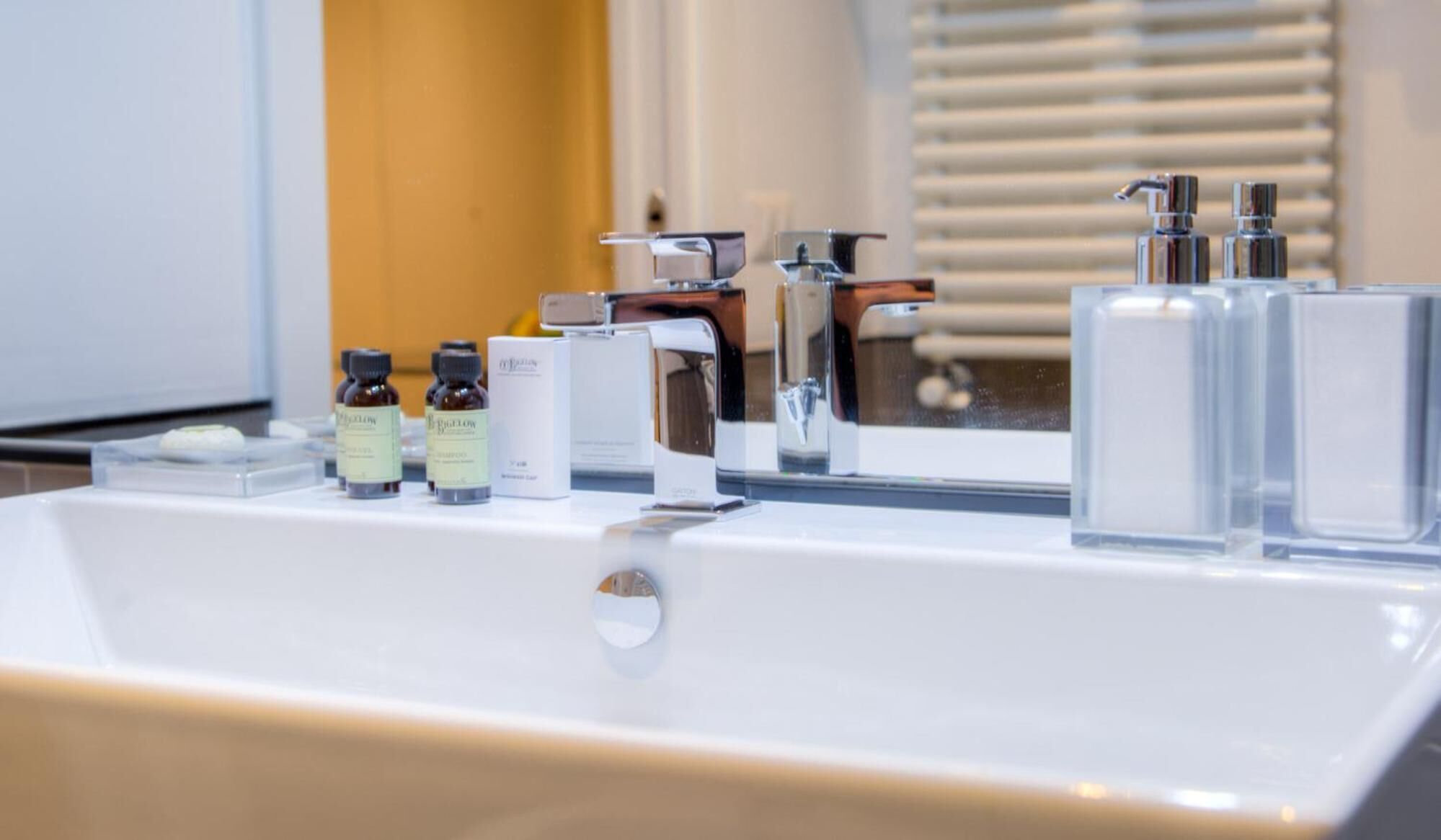Ein modernes Badezimmer mit einem weißen Waschbecken, chromfarbenen Armaturen und einem Spiegel.