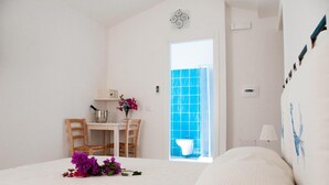 A hotel room with a bed, a small table with chairs, a vase with flowers, a window with blue tiles, and a wall-mounted light fixture. - Métà hotel (Santa Teresa di Gallura)