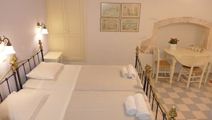 Una cama doble con sábanas blancas, una mesita de noche pequeña, una silla, un escritorio con silla, una lámpara de pared y un suelo a cuadros.