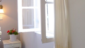 Una habitación con un ventanal grande, una mesa pequeña con una planta en maceta y un cuadro en la pared.